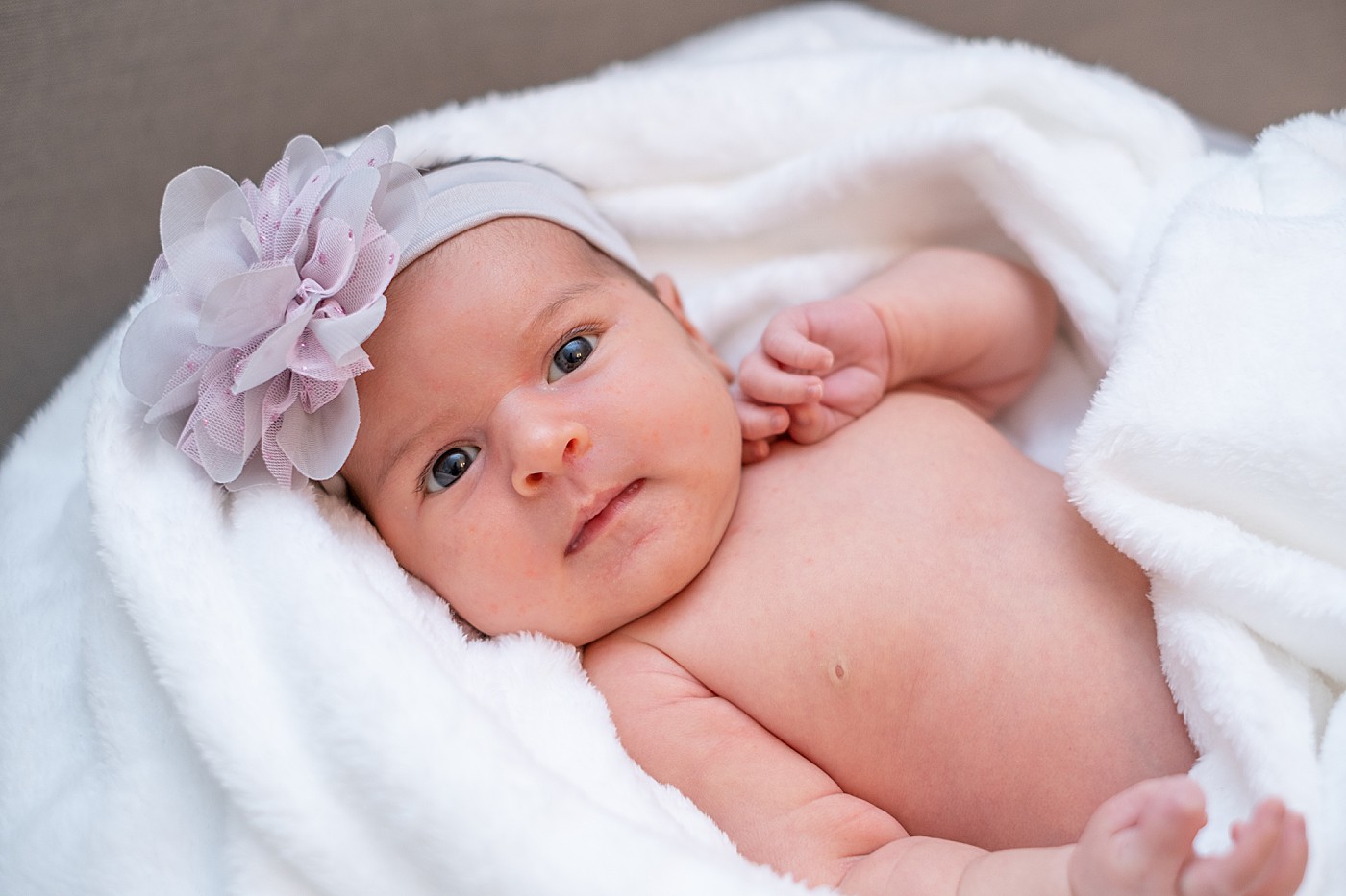 Baby wrapped in white blanket with a flower bow.