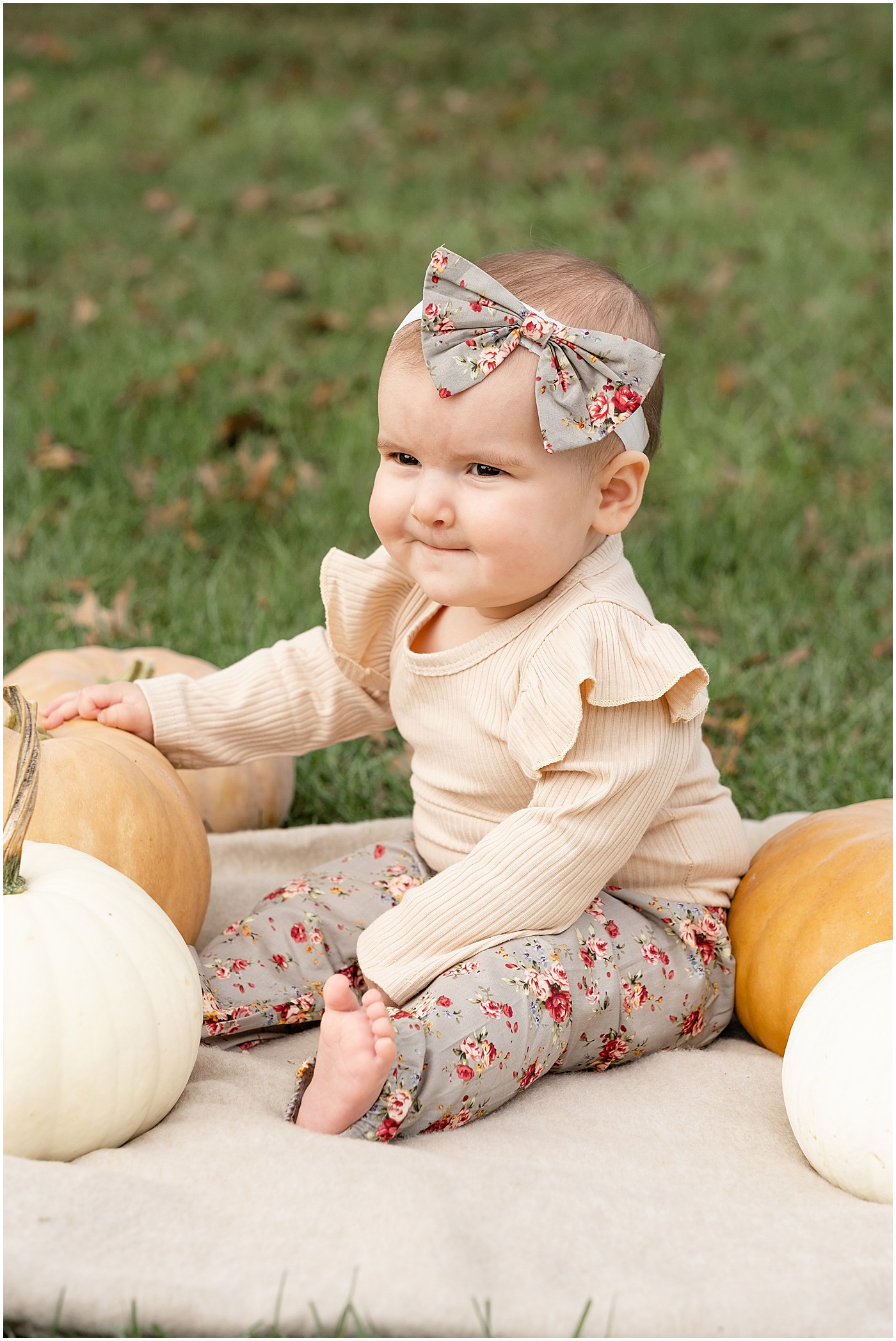 a baby smiling while she is holding pumpkins for her first autumn photos