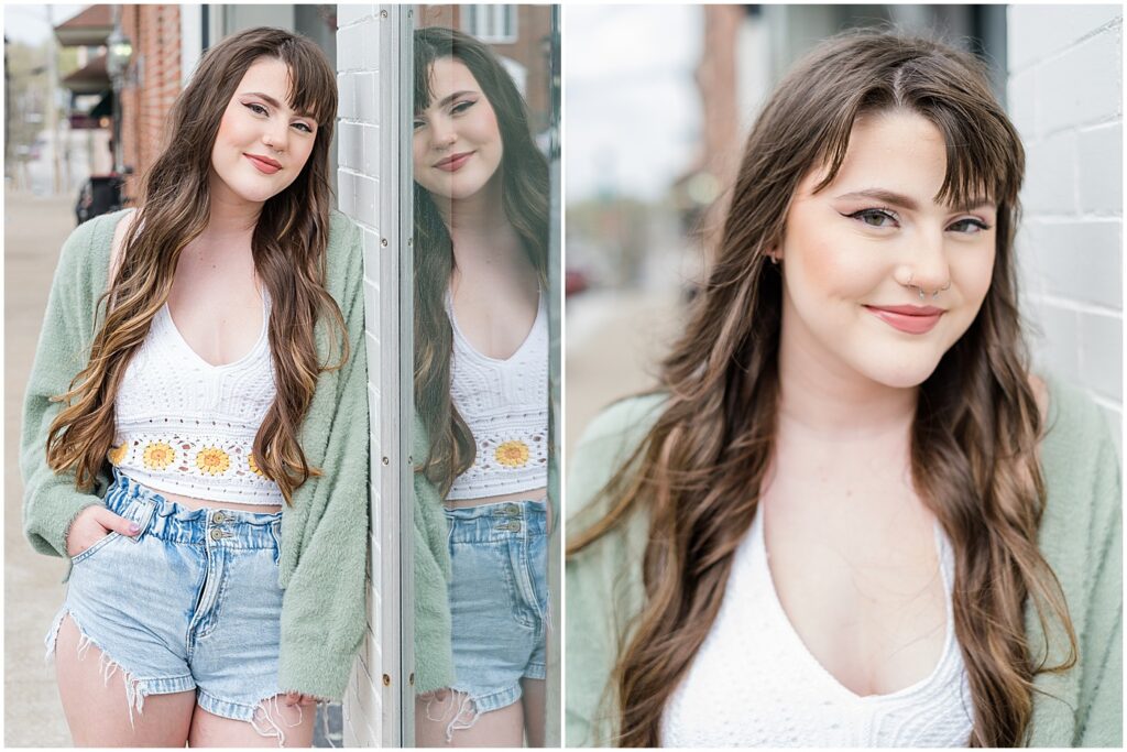 senior girl in shorts and green sweater leaning against downtown shop window