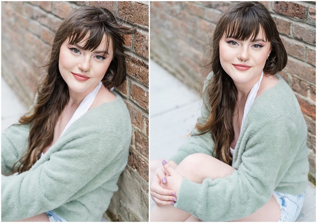 a senior girl in a green sweater posing in front of a brick wall