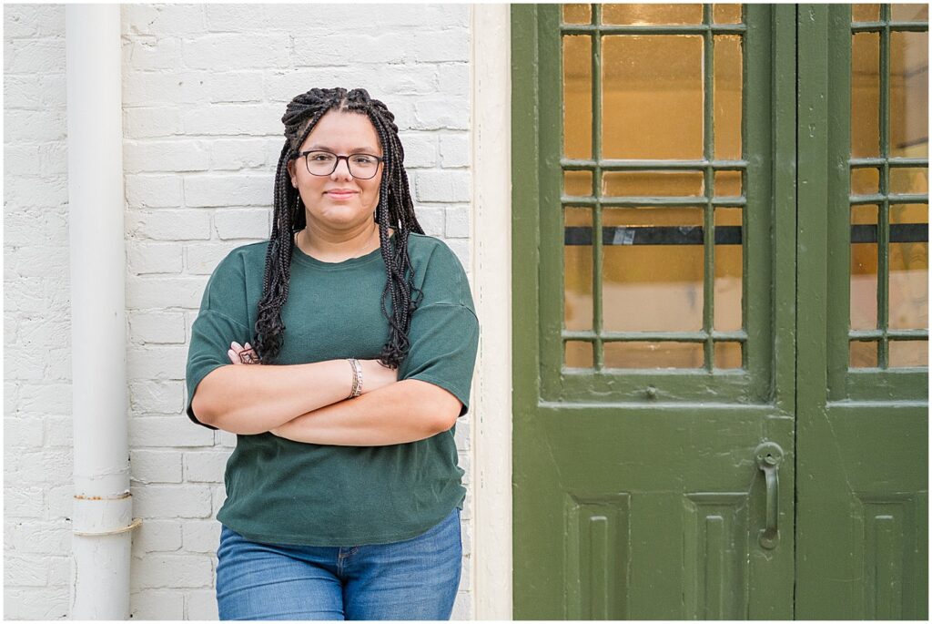 senior girl in green tee shirt crossing her arms by a green door