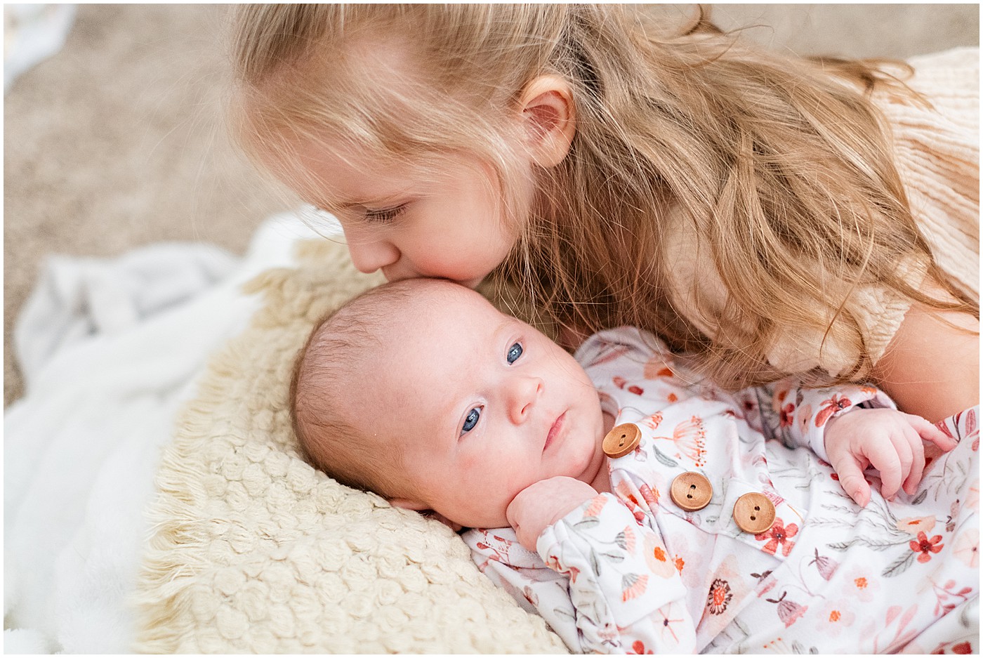 toddler with long blond hair kissing newborn sister