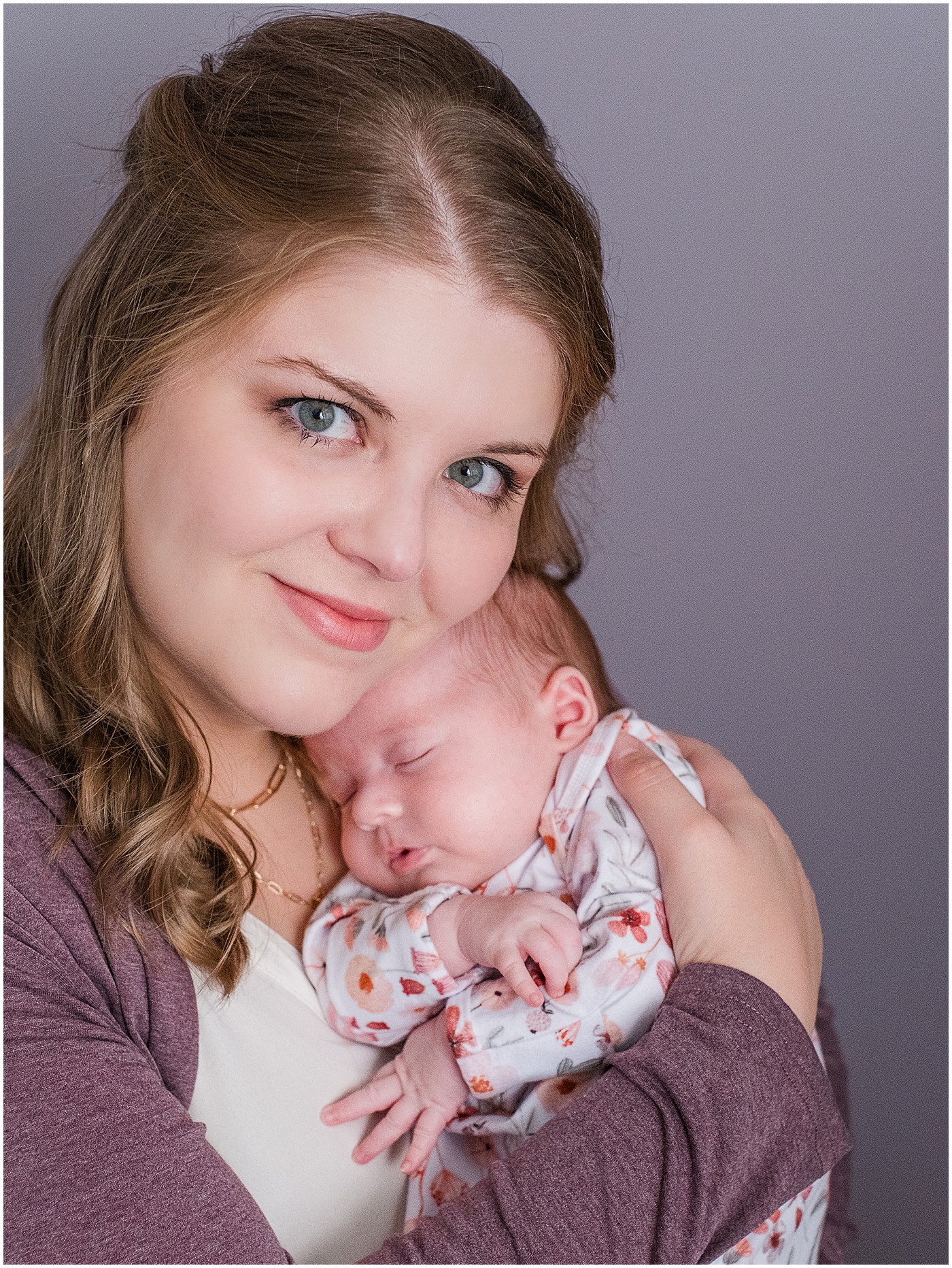 mother cuddles sleeping newborn and smiles at camera