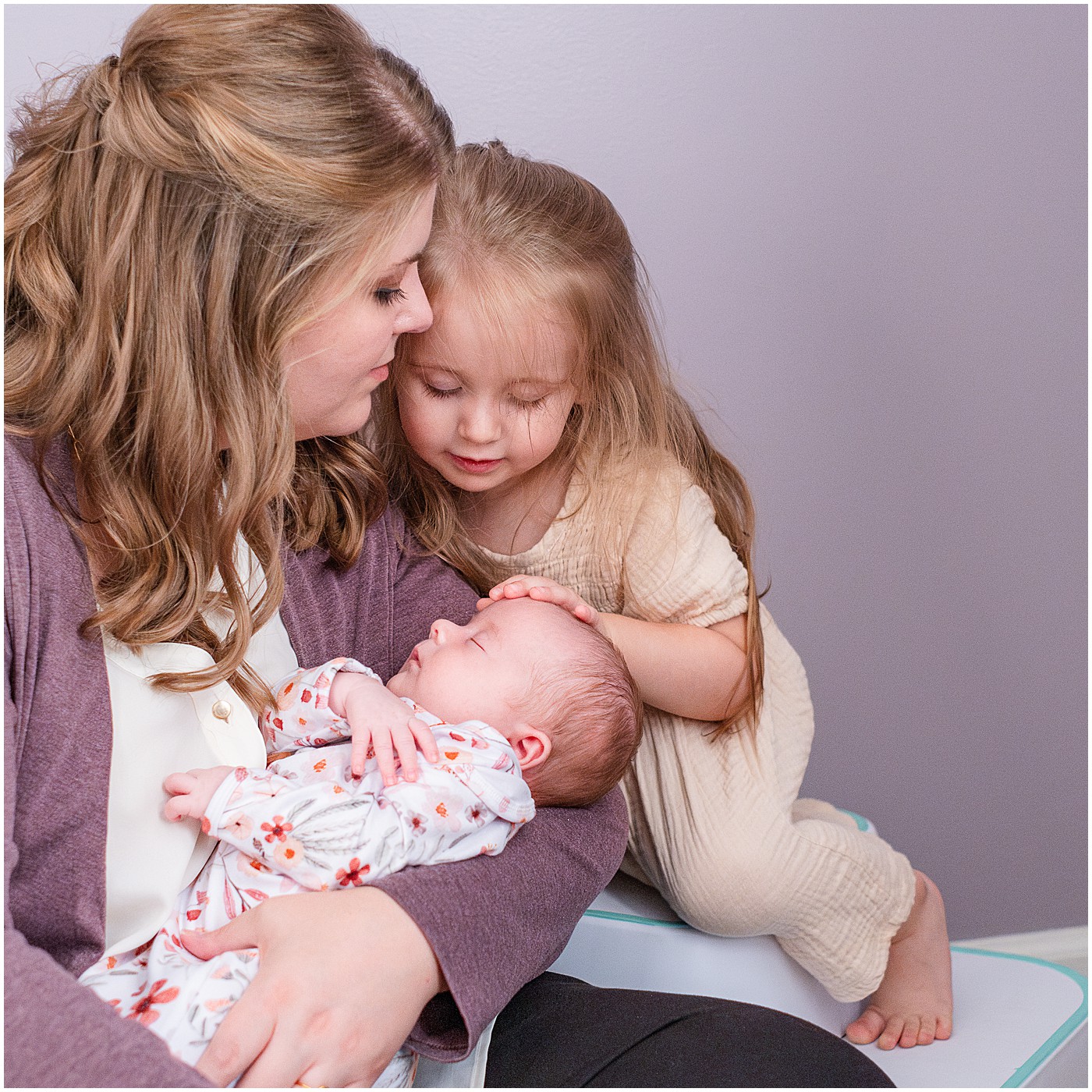 a toddler reaching down touching her newborn sister's head in this mommy and me session