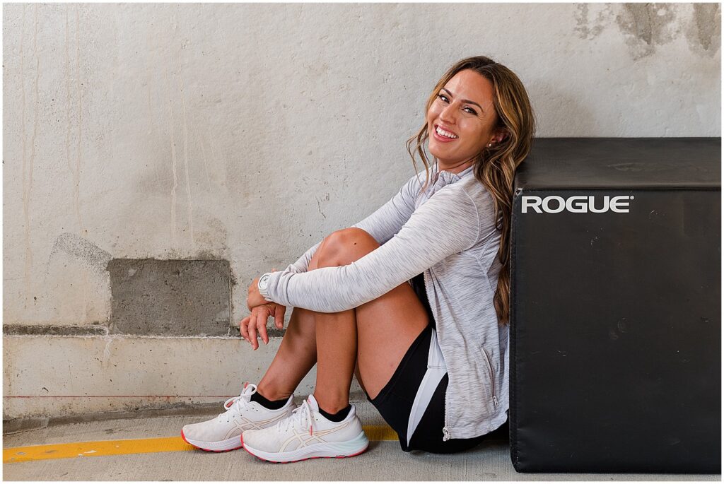 brand image of Yvonne in workout sitting on floor leaning against workout box while smiling at camera