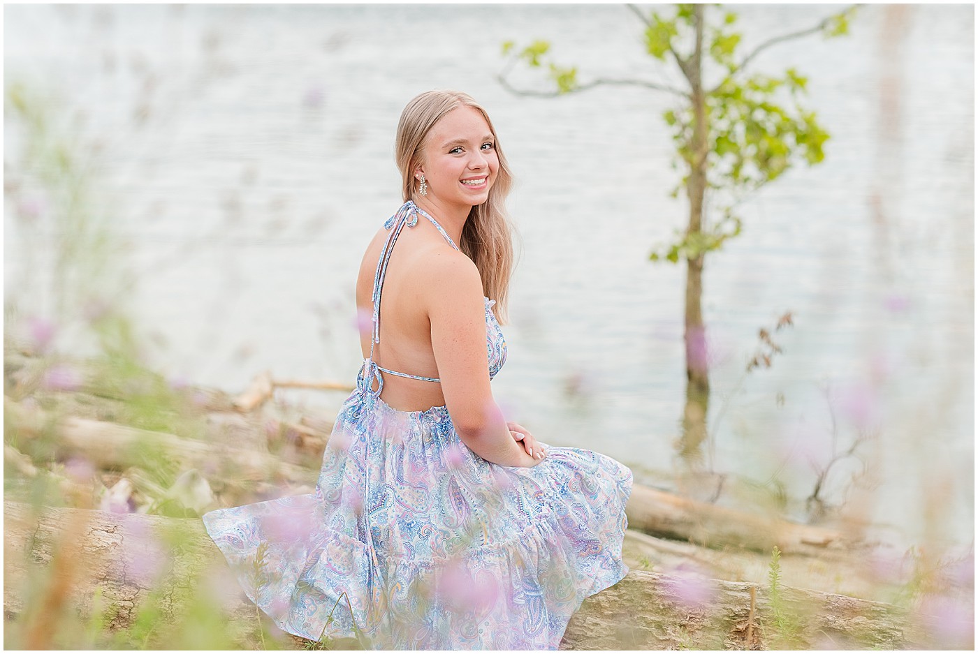 over the shoulder pose of a 2025 senior sitting on a log with purple flowers in the foreground